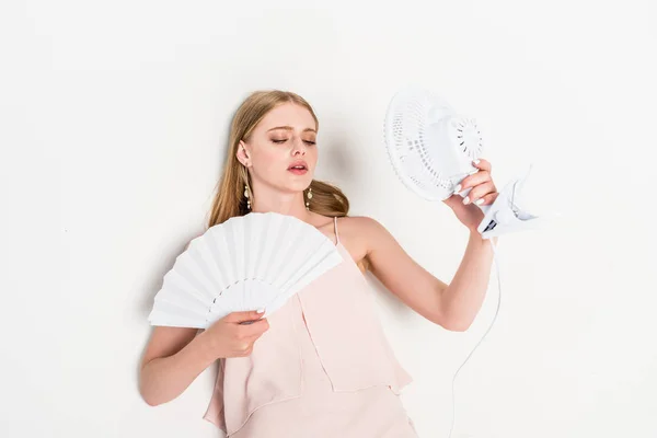 Draufsicht der schönen jungen Frau mit elektrischem Ventilator und Handventilator, die unter Hitze auf Weiß leidet — Stockfoto