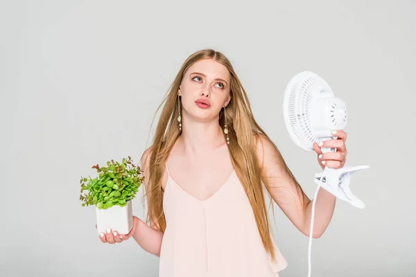 Bella giovane donna con ventilatore elettrico e vaso da fiori che soffre di calore isolato su grigio — Foto stock