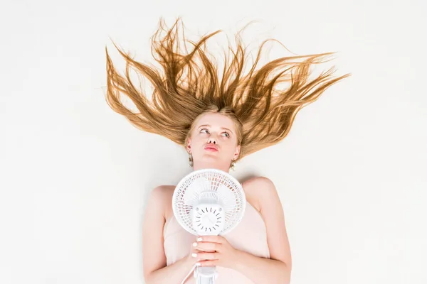 Vue de dessus de la fille tenant ventilateur électrique tout en souffrant de chaleur sur blanc — Photo de stock