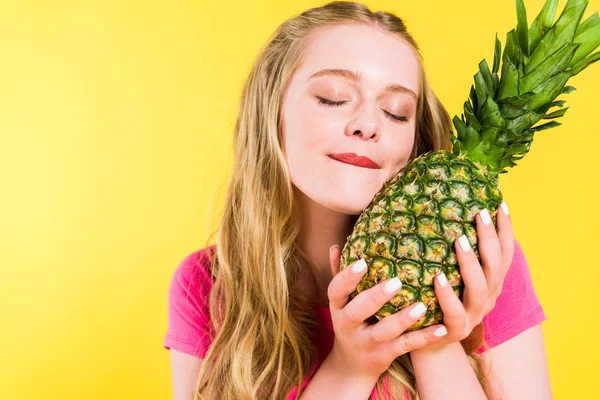 Bela menina mordendo lábio e posando com abacaxi isolado no amarelo — Fotografia de Stock