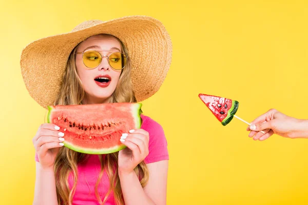 Bella ragazza sorpresa in cappello di paglia con anguria guardando lecca-lecca isolato su giallo — Foto stock