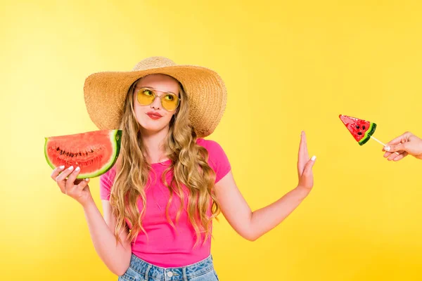 Dissatisfied girl with watermelon gesturing and refusing lollipop on yellow — Stock Photo