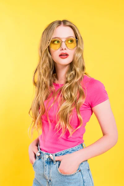 Belle fille blonde en lunettes de soleil avec les mains dans les poches Isolé Sur jaune — Photo de stock