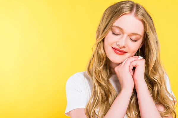 Bella bionda giovane donna con gli occhi chiusi e le mani incrociate isolato su giallo — Foto stock