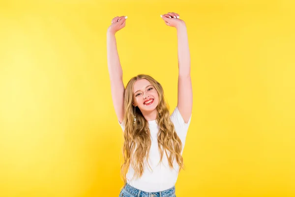 Красива щаслива блондинка молода жінка з піднятими руками ізольовані на жовтому — стокове фото