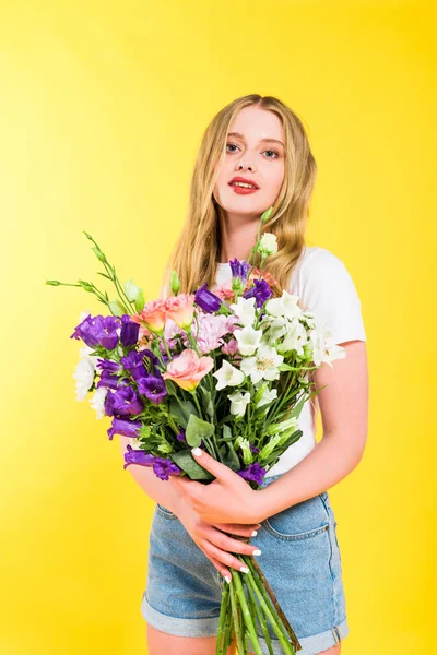 Attraktives blondes Mädchen mit Blumen blickt in die Kamera auf gelb — Stockfoto