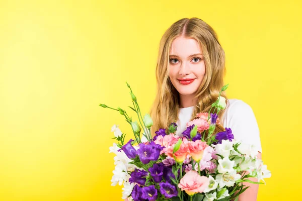 Linda menina loira com flores olhando para a câmera em amarelo — Fotografia de Stock