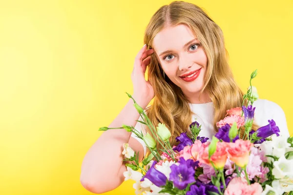 Schöne lächelnde blonde Mädchen mit Blumen, die das Haar auf gelb berühren — Stockfoto