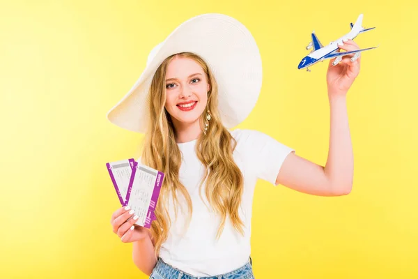 Beautiful girl with plane model and air tickets On yellow — Stock Photo