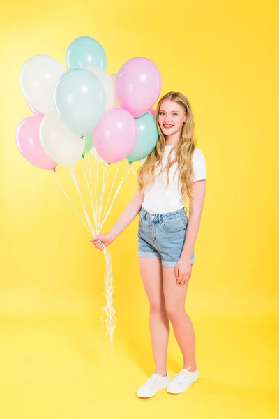 Красива дівчина з повітряними кулями дивиться на камеру і посміхається На жовтому — стокове фото