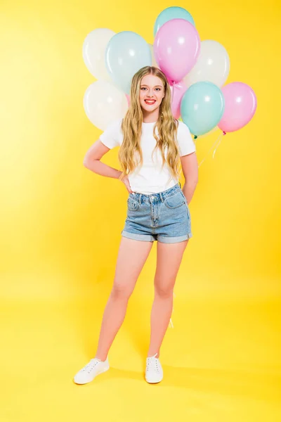 Красивая улыбающаяся девушка с воздушными шарами на желтом — стоковое фото