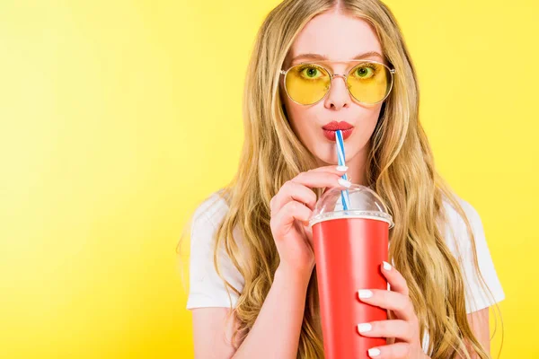 Beautiful girl in sunglasses holding drink in disposable cup On yellow — Stock Photo