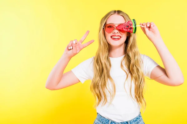 Beautiful happy girl in sunglasses with lollipop in shape of watermelon doing Peace Sign On yellow — Stock Photo