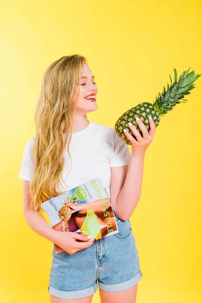 Schöne Mädchen mit Schönheit und Stil Magazin und Ananas isoliert auf gelb — Stockfoto