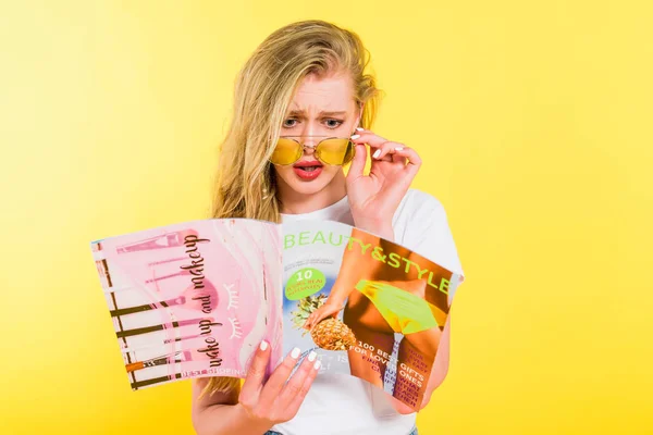 Hermosa chica sorprendida leyendo belleza y estilo revista aislado en amarillo - foto de stock