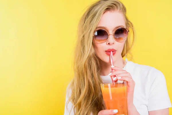 Hermosa chica en gafas de sol beber cóctel aislado en amarillo - foto de stock