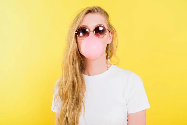 Hermosa chica en gafas de sol soplando goma de mascar aislado en amarillo - foto de stock