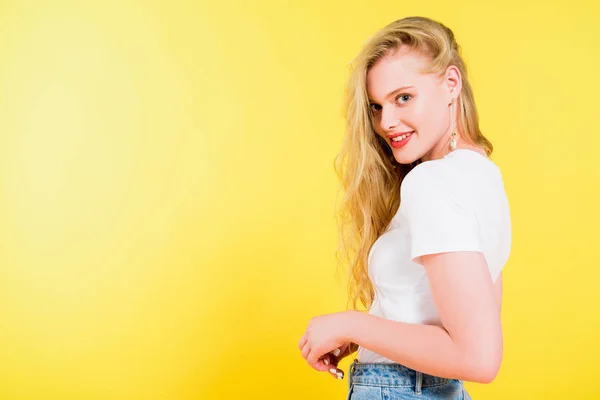 Schöne lächelnde blonde junge Frau blickt in die Kamera auf gelb — Stockfoto