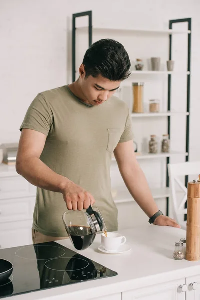 Schöner asiatischer Mann gießt Kaffee in Tasse aus Kaffeekanne in Küche — Stockfoto