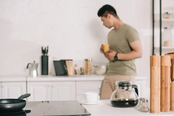 Foco seletivo de jovem asiático homem segurando vidro com suco de laranja na cozinha — Fotografia de Stock