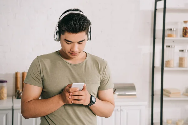 Junger asiatischer Mann benutzt Smartphone während er Musik über Kopfhörer hört — Stockfoto