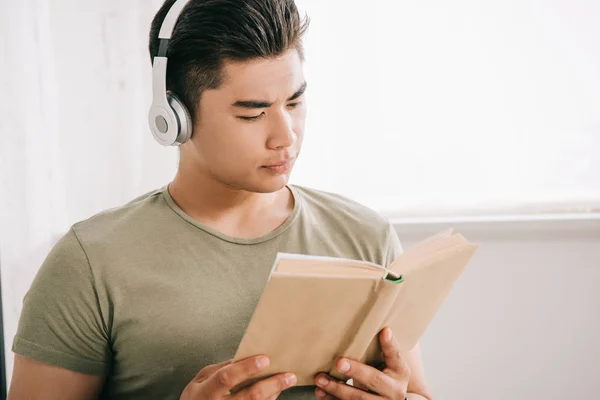 Jovem asiático homem leitura livro enquanto ouvir música em fones de ouvido — Fotografia de Stock