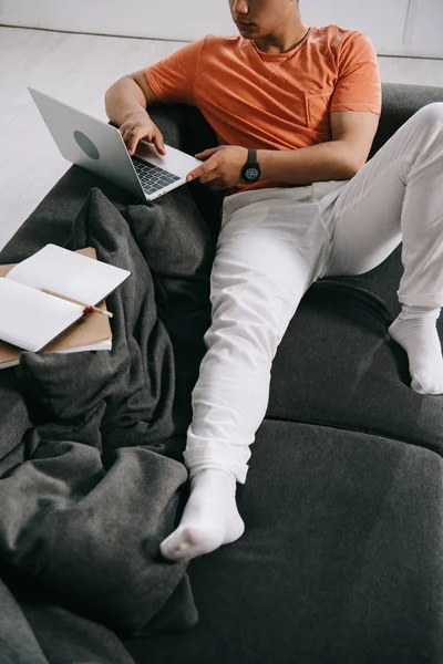 Cropped view of young man lying on sofa and using laptop at home — Stock Photo
