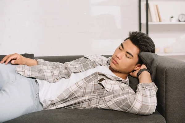 Young, exhausted asian man in plaid shirt sleeping on sofa at home — Stock Photo