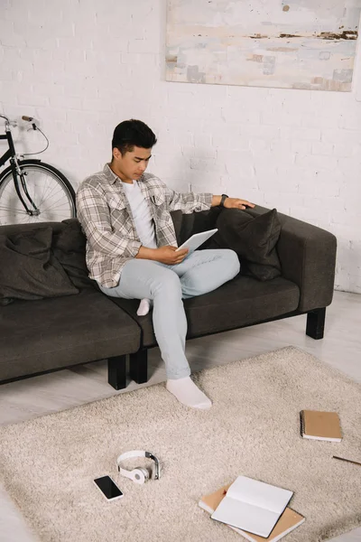 Young asian man sitting on sofa at home and using digital tablet — Stock Photo