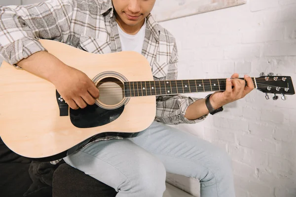 Обрізаний вид на молодого чоловіка, який грає на акустичній гітарі вдома — стокове фото