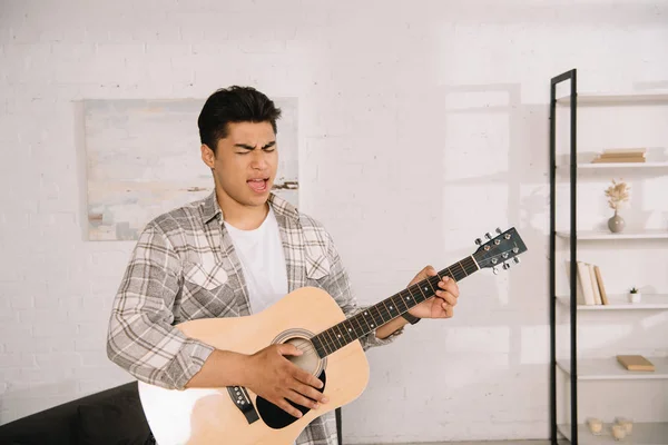 Красивий азіатський чоловік грає на акустичній гітарі і співає вдома — стокове фото