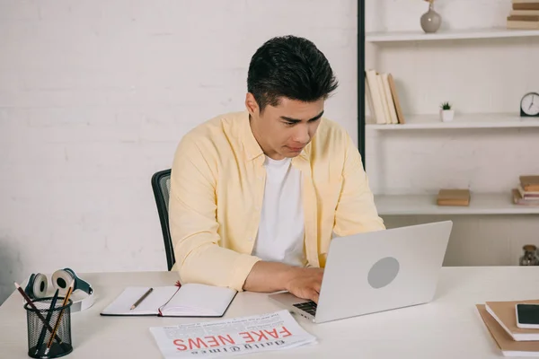 Concentrado asiático hombre sentado en escritorio y usando portátil en casa - foto de stock