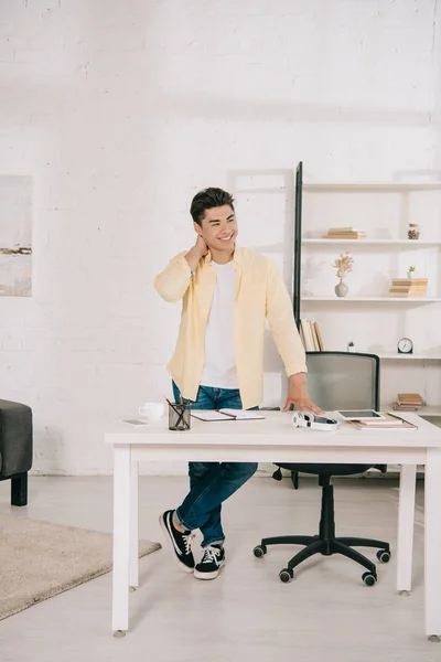 Beau, souriant asiatique homme debout près de la table à la maison et regardant loin — Photo de stock