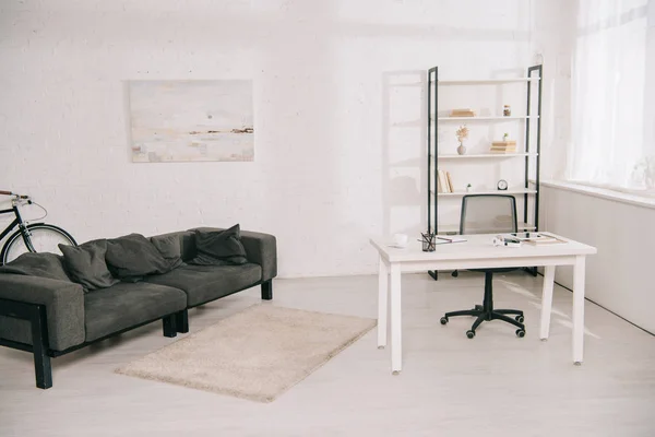 Просторная гостиная с серым диваном, белым столом и стойкой с книгами — стоковое фото