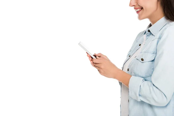 Vista lateral de una joven sonriente usando un teléfono inteligente aislado en blanco - foto de stock