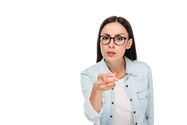 Chica morena enojada en gafas en chaqueta de mezclilla apuntando con el dedo a la cámara aislada en blanco - foto de stock