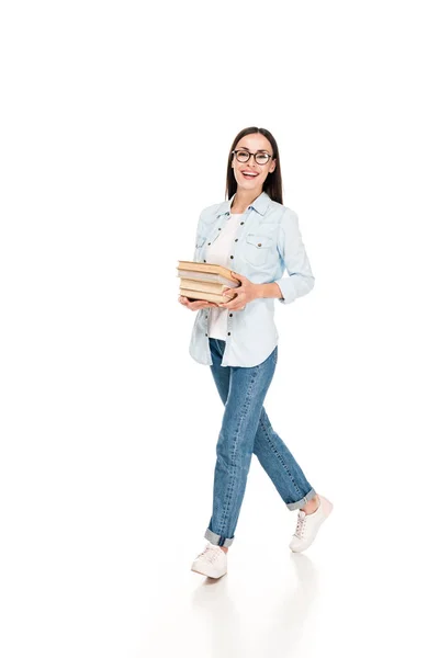 Heureuse fille brune dans des lunettes en jean veste marche avec des livres isolés sur blanc — Photo de stock