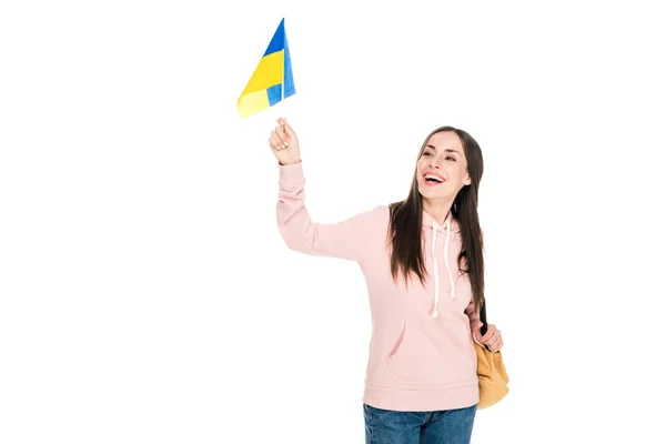 Sonriente chica morena con mochila sosteniendo bandera ucraniana aislada en blanco - foto de stock