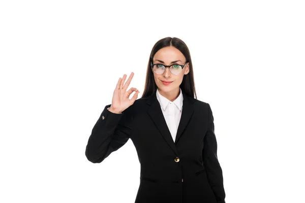 Усміхнена бізнес-леді в чорному костюмі, що показує знак ОК ізольовано на білому — стокове фото