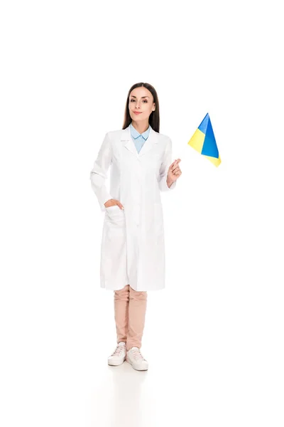 Полный вид улыбающегося врача в белом халате, держащего украинский флаг изолированным на белом — стоковое фото