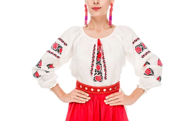 Обрезанный вид молодой женщины в национальном украинском костюме стоящей с руками на бедрах изолированной на белом — стоковое фото