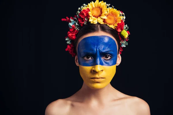 Triste mujer joven desnuda en corona floral con bandera ucraniana pintada en piel aislada en negro - foto de stock