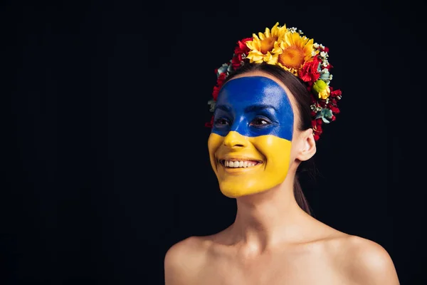 Happy naked young woman in floral wreath with painted Ukrainian flag on skin isolated on black — Stock Photo