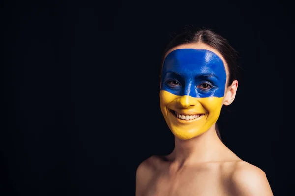 Giovane donna nuda con bandiera ucraina dipinta su pelle sorridente isolata su nero — Foto stock