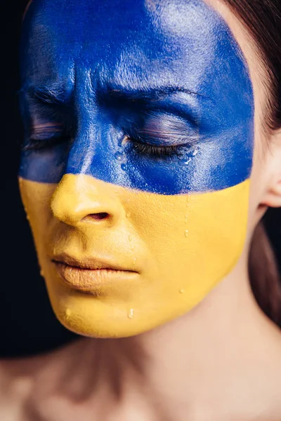 Vue rapprochée de la jeune femme avec drapeau ukrainien peint sur la peau pleurer isolé sur noir — Photo de stock