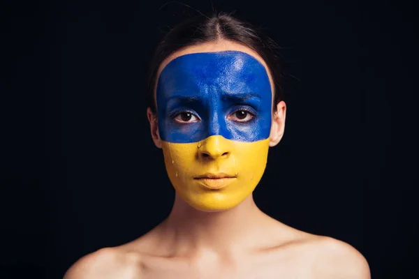 Naked young woman with painted Ukrainian flag on face isolated on black — Stock Photo