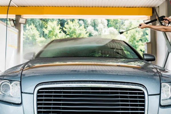 Cropped view of cleaner standing and washing grey automobile outside — Stock Photo