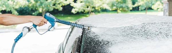 Panoramic shot of man holding pressure washer with foam near car — Stock Photo