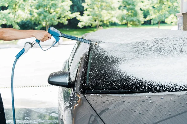 Vue recadrée de la laveuse de voiture tenant la laveuse sous pression avec mousse près de la voiture — Photo de stock