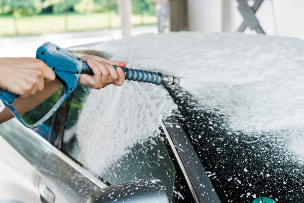 Vista ritagliata di pulitore auto tenuta rondella di pressione con schiuma vicino auto — Foto stock